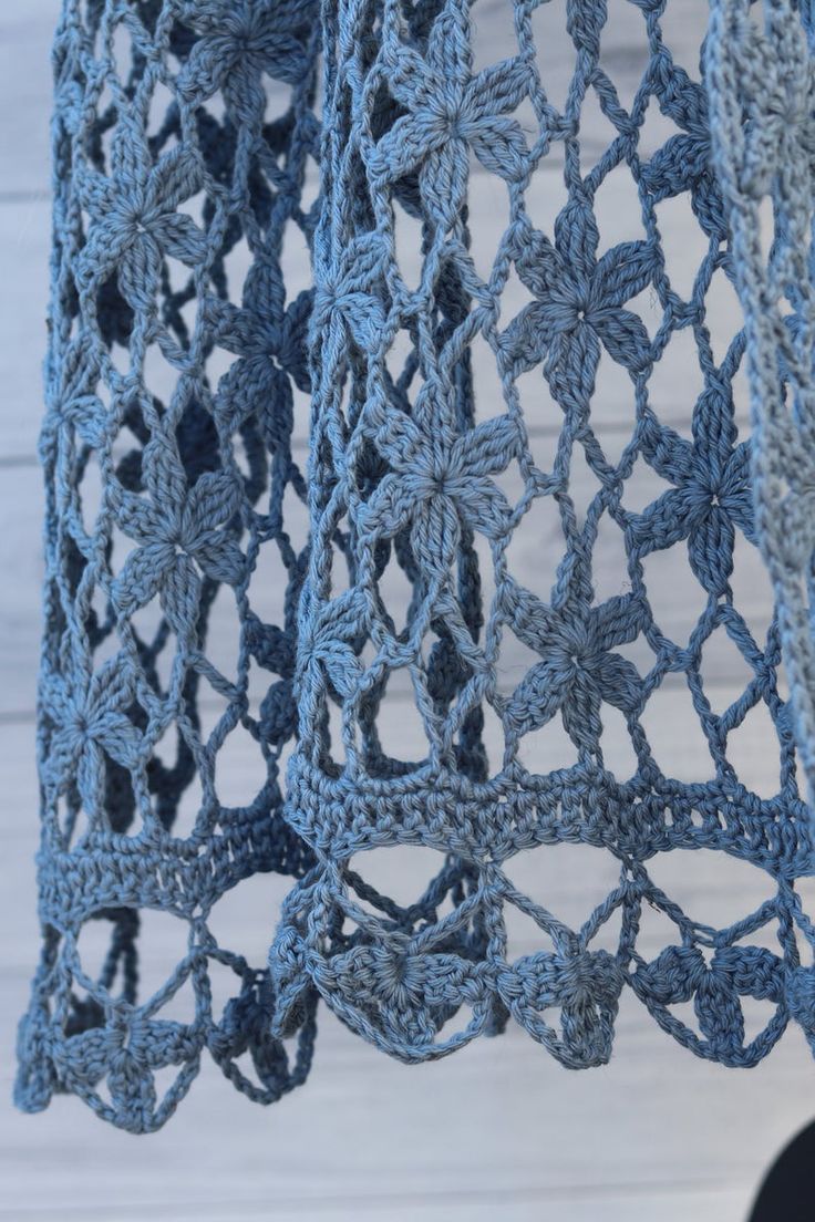 a blue crocheted shawl hanging from a hook on a white wooden wall