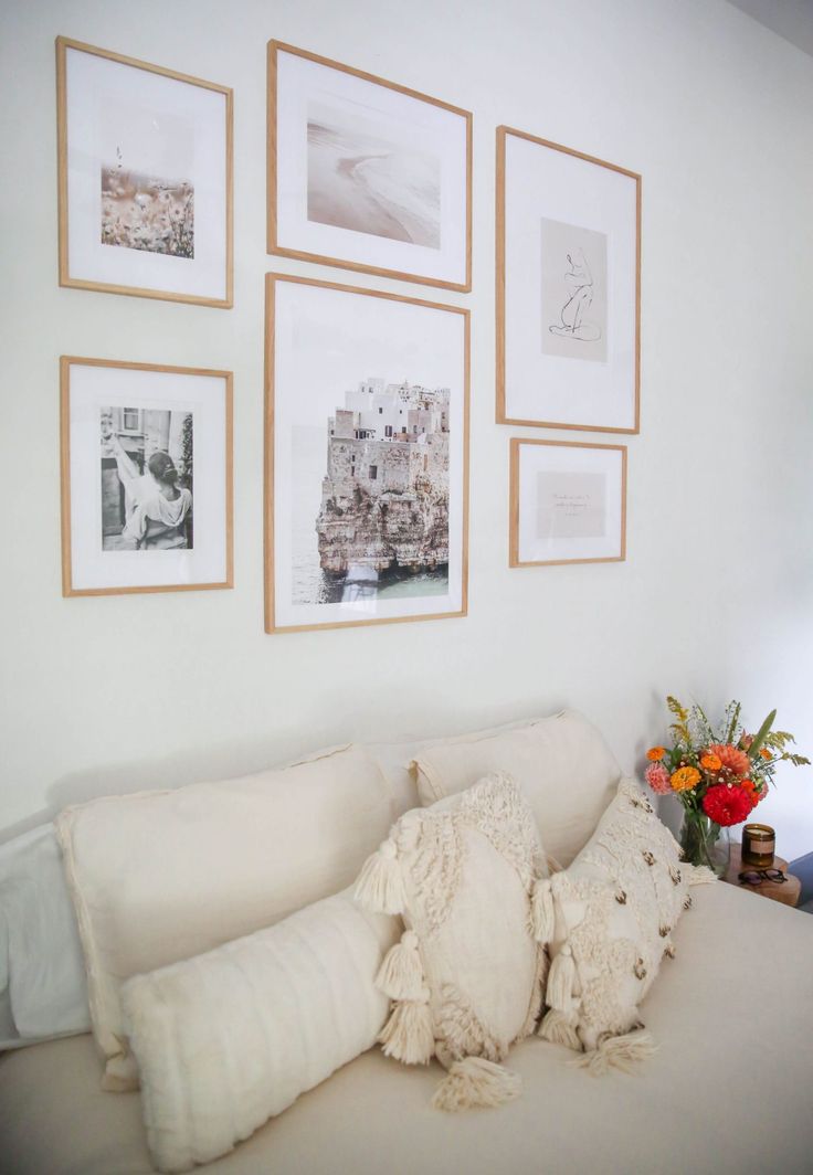 a white couch with pillows and pictures on the wall above it, along with vases filled with flowers