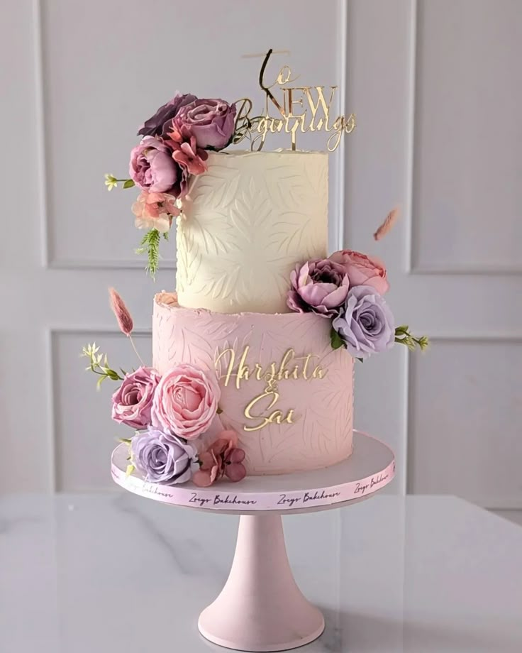 a three tiered cake decorated with flowers and gold lettering that says new beginnings on the side