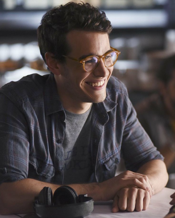 a man sitting at a table with headphones in his hand and smiling for the camera