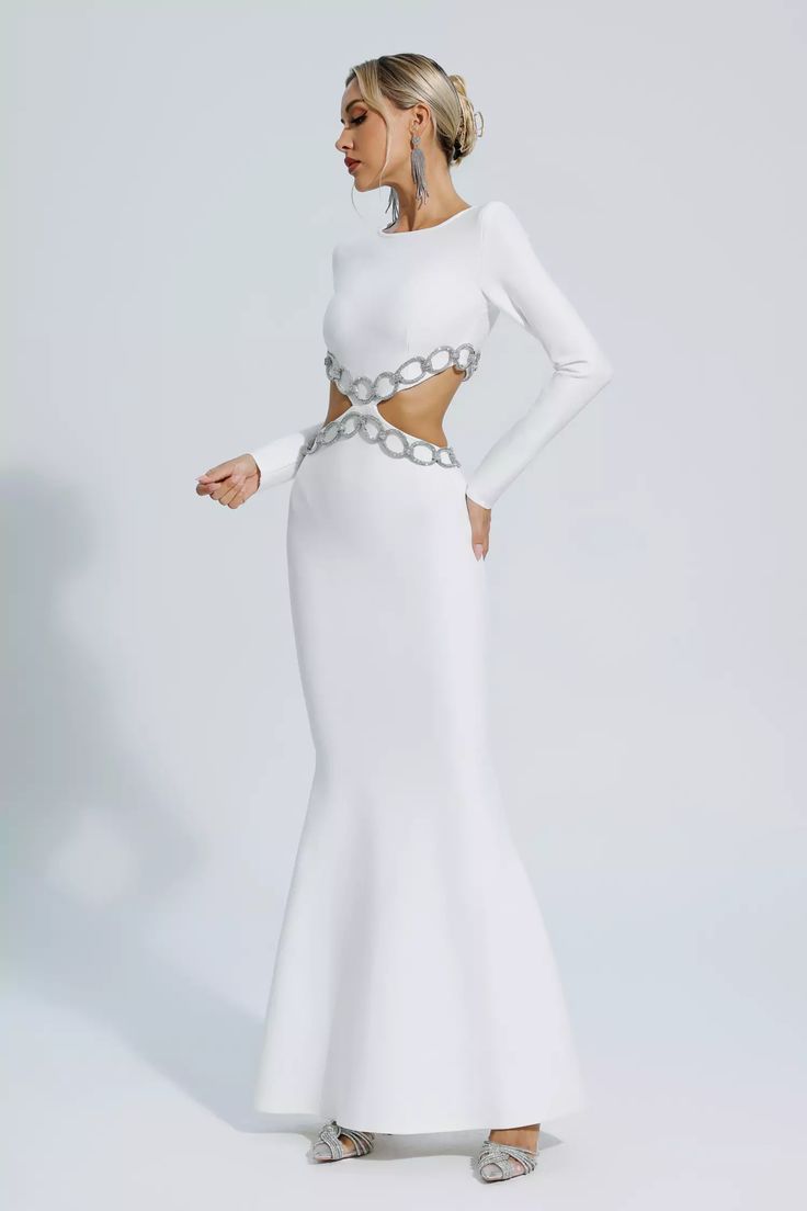 a woman wearing a white dress with chains on the waist and long sleeves, standing in front of a white background