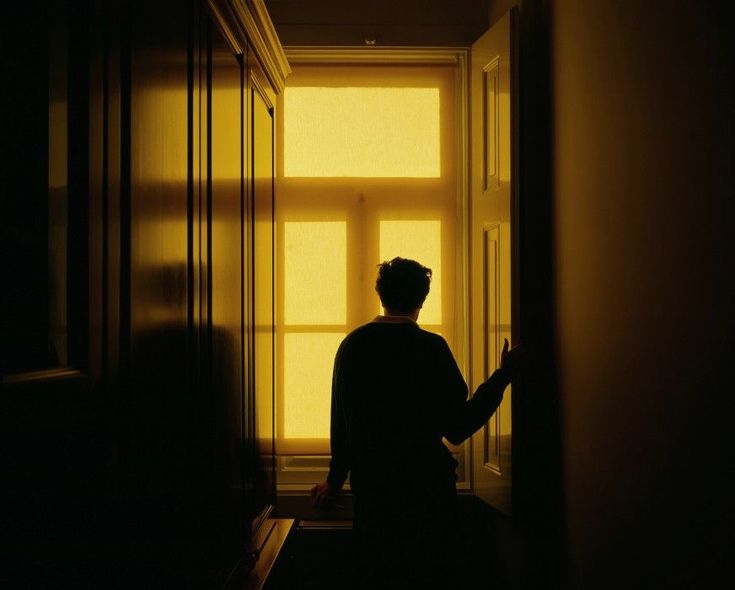 a person standing in an empty hallway with the sun shining through the window behind them