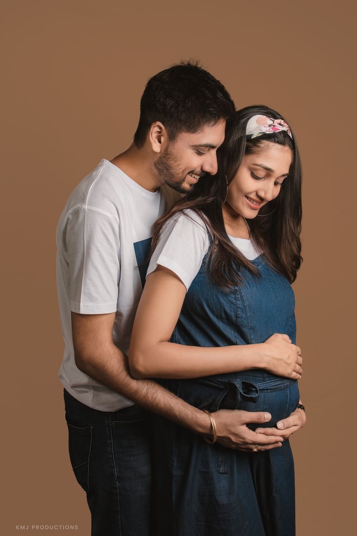 a man and woman standing next to each other with their arms around the pregnant belly