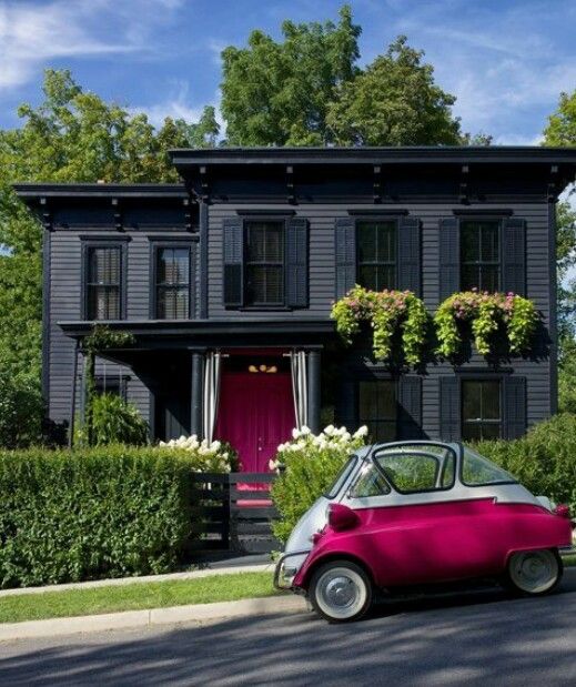 a pink car is parked in front of a black house with flowers on the windows