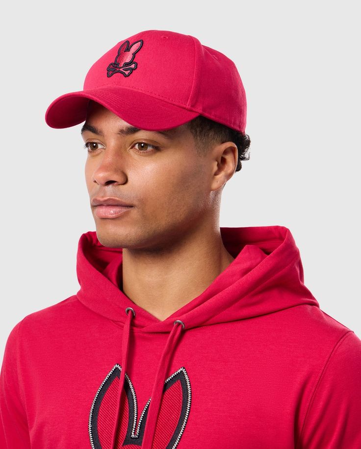 A person wearing the Psycho Bunny MENS WALTER BASEBALL CAP - B6A800D200 and a matching red hoodie with a bunny logo, looking to the side against a plain background. The durable and comfortable cap is crafted from 100% cotton, perfectly complementing the casual outfit. Sporty Cotton Snapback Hat For Baseball Season, Bunny Man, Bunny Logo, Style Guides, Baseball Cap, In Style, Mens Accessories, Baseball, Size Medium