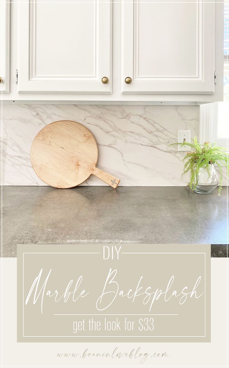 a white kitchen with marble backsplash and wooden paddle on the counter top next to a potted plant