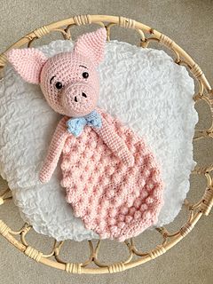 a pink knitted pig laying on top of a white blanket in a wicker basket