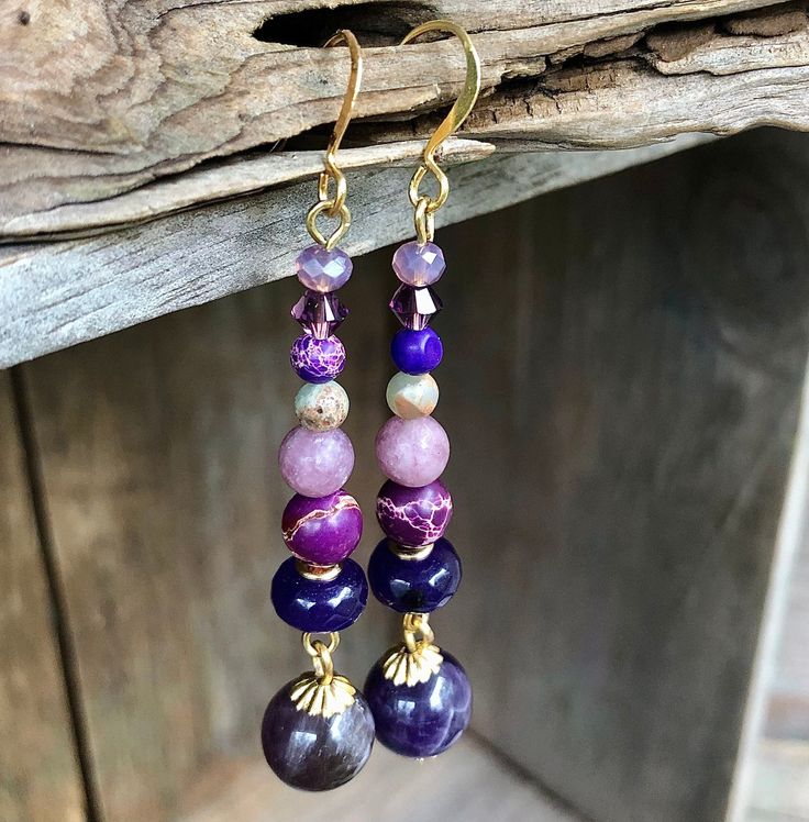 "Take a look at these beautiful 2 inch purple and grey/green Snakeskin Jasper, purple Amethyst, and Quartz Crystal earrings with Gold accents! These earrings are simply stunning and will elevate any outfit you wear them with. The combination of the purple and grey/green Snakeskin Jasper, purple Amethyst, and Quartz Crystal beads creates a unique and eye-catching look. The Gold accents add a touch of elegance and sophistication to these already stunning earrings. These earrings would look amazing with elegant evening attire at a fancy soiree, but they would also be perfect for a casual, informal look at a kids' baseball game. They are versatile and can be dressed up or down, depending on the occasion. If you're looking to complete your look, coordinating bracelet and necklace are available Beaded Amethyst Earrings Gift, Beaded Amethyst Earrings For A Gift, Amethyst Beaded Earrings As Gift, Purple Round Spiritual Earrings, Spiritual Round Purple Earrings, Spiritual Purple Round Earrings, Purple Beaded Amethyst Earrings, Purple Amethyst Beaded Earrings, Handmade Amethyst Purple Earrings