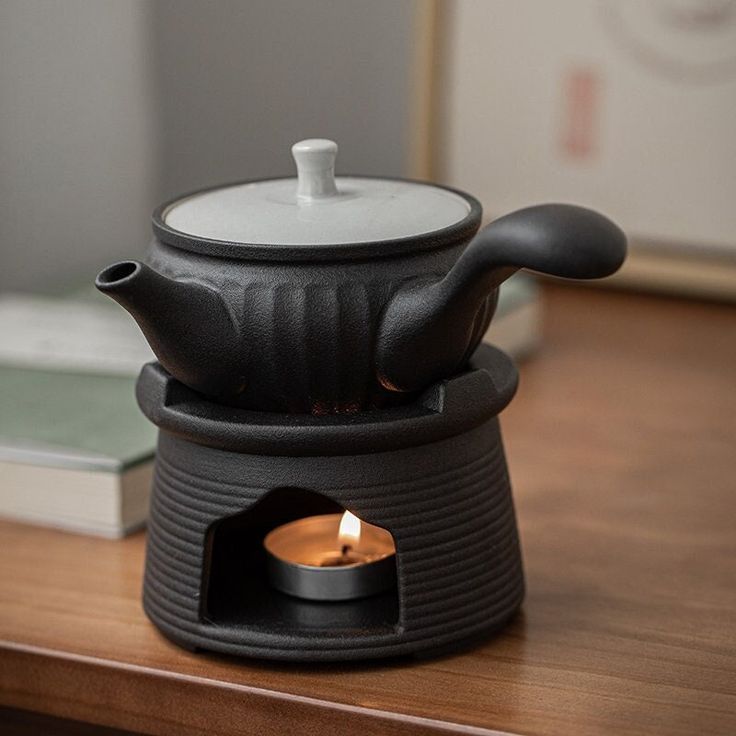 a small stove with a lit candle in it on a wooden table next to a book