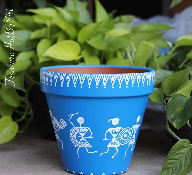 a blue planter with white designs on it next to some green leaves and plants