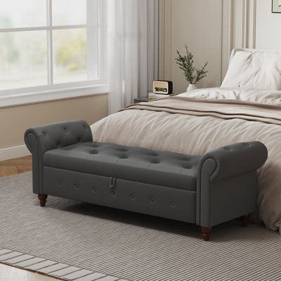 a bed with a gray tufted upholstered bench in front of the window