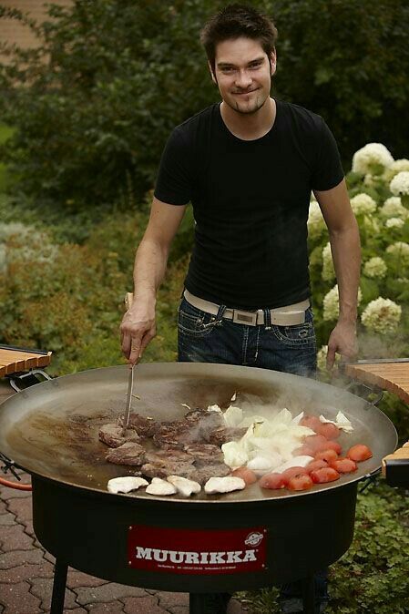 a man standing next to a large grill with food cooking on it's side