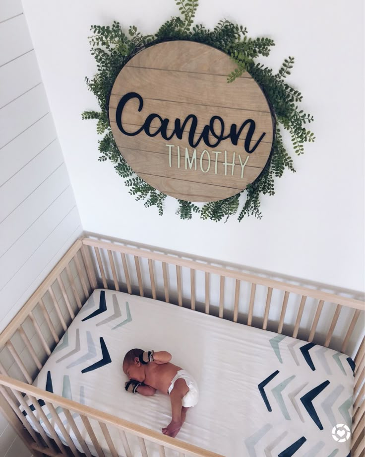 a baby laying in a crib next to a wooden sign