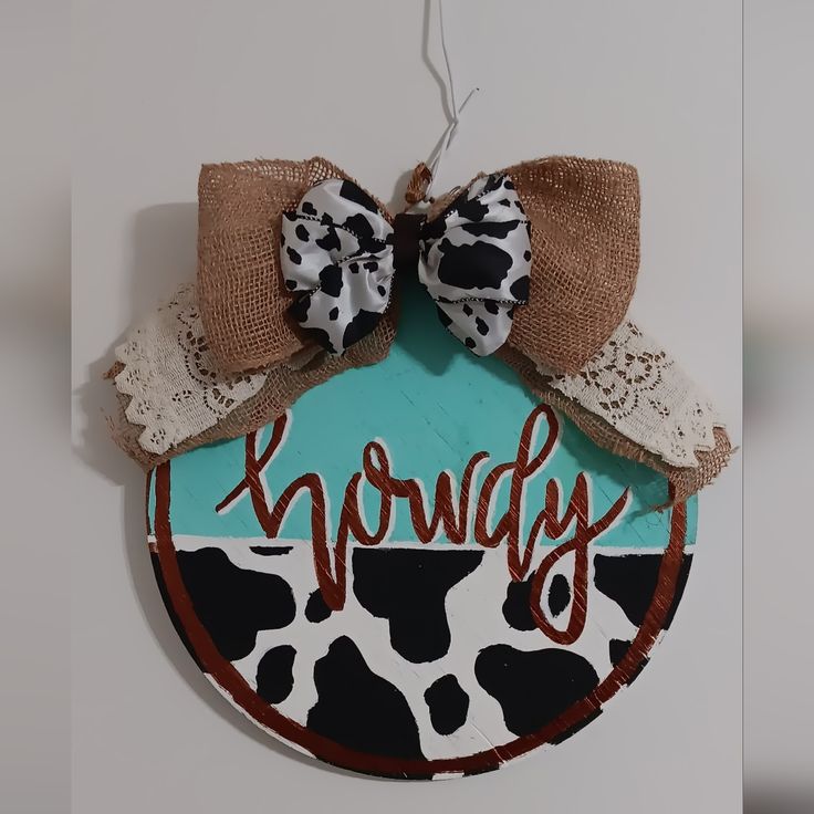 a cow print sign hanging from the side of a wall with a bow on it