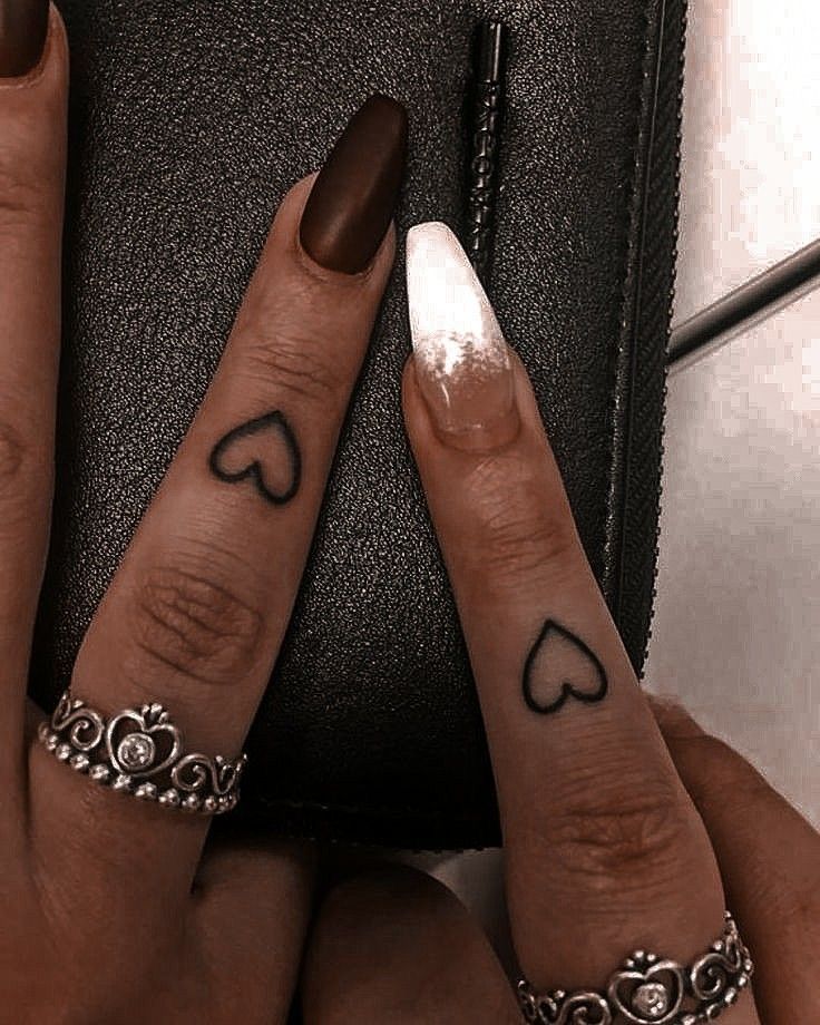 two fingers with hearts on them are next to a black purse and one has a ring