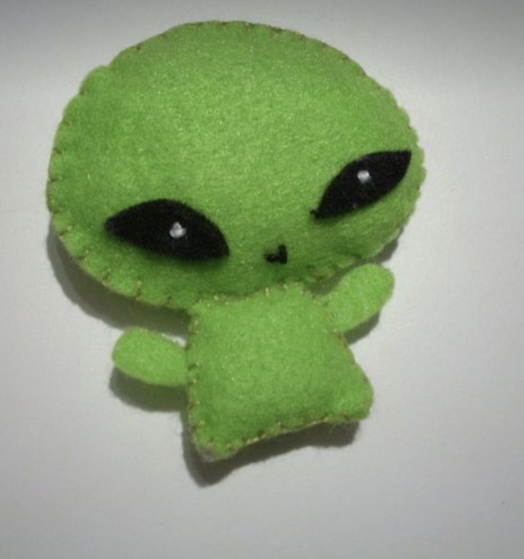 a small green stuffed animal with black eyes and an alien like head, sitting on a white surface