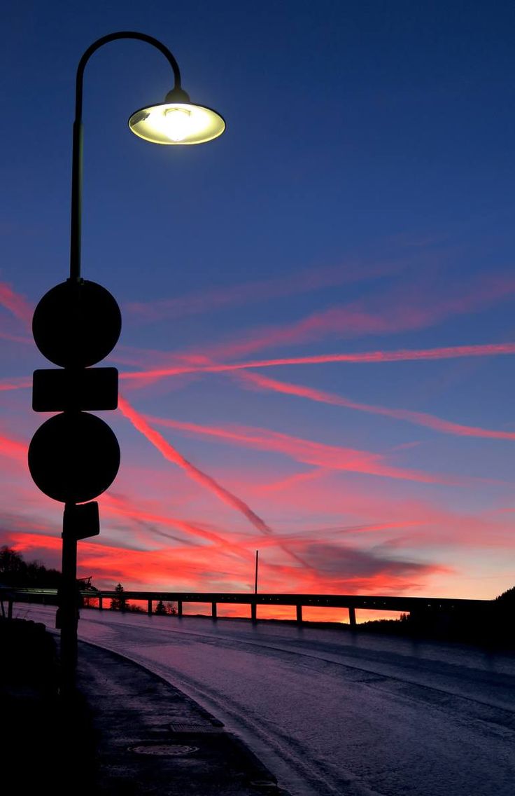 a street light sitting on the side of a road next to a bridge at sunset