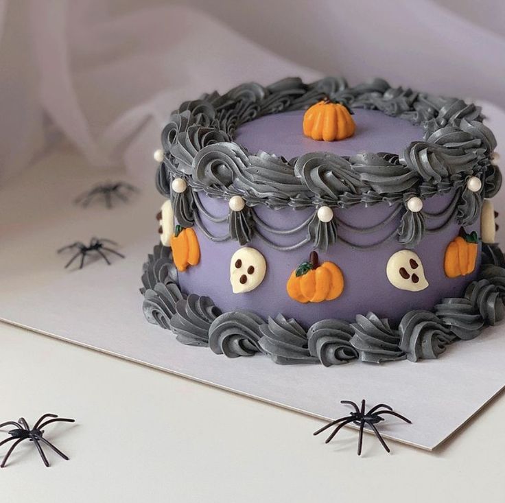 a purple cake decorated with halloween decorations on top of a white table next to black spider webs