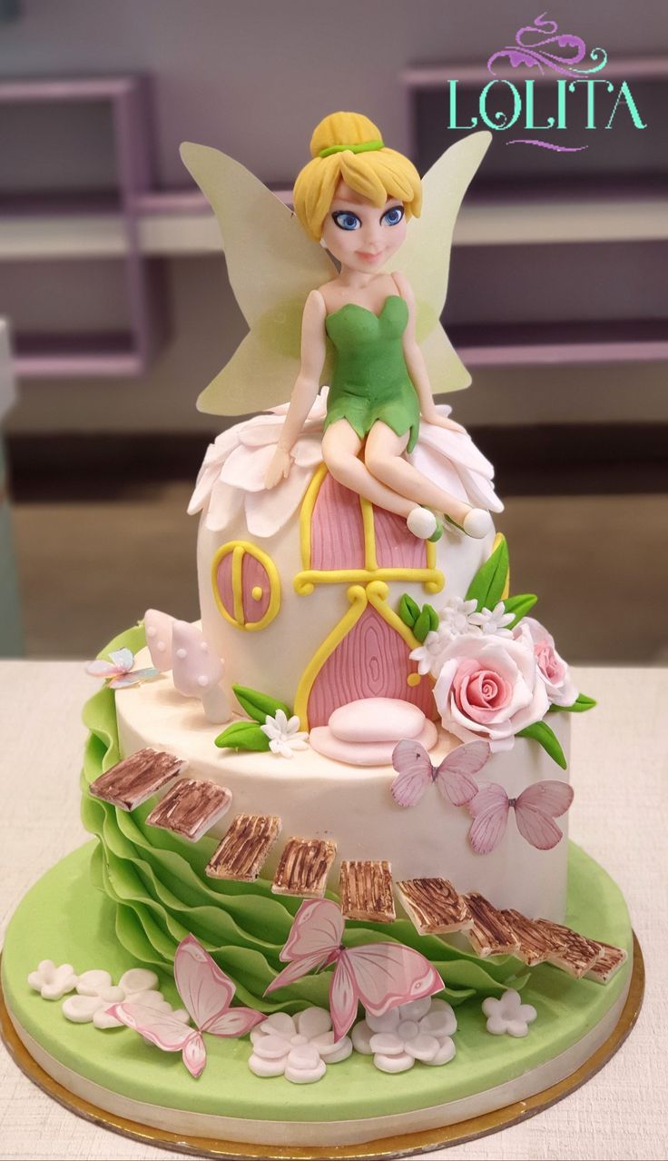 a cake decorated with a fairy sitting on top of a green base and pink flowers