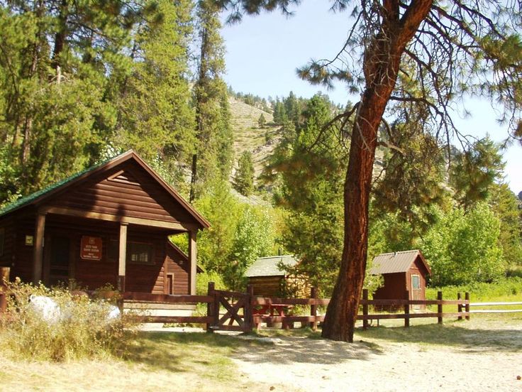 two cabins in the woods next to each other with trees and grass on either side