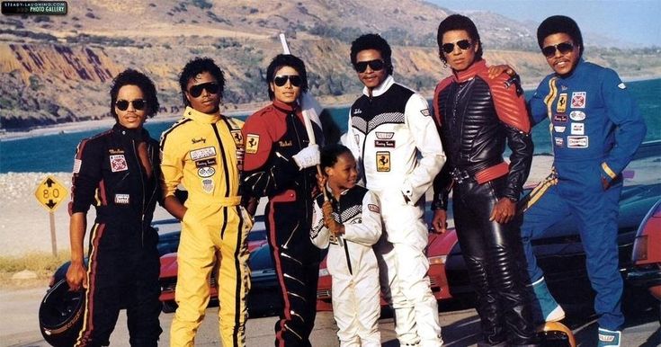 a group of people standing next to each other in front of a car with mountains in the background