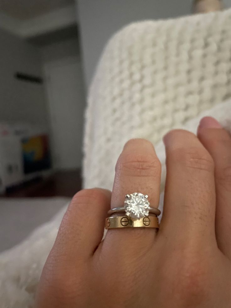 a woman's hand holding a diamond ring in her left hand, with the other hand on top of it