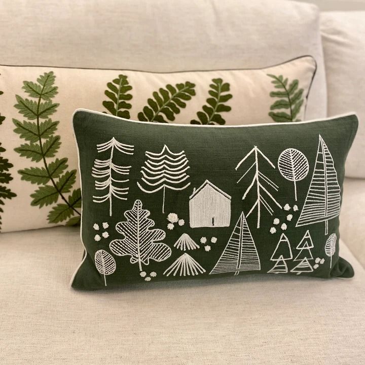 a green pillow sitting on top of a white couch next to pillows with trees and houses