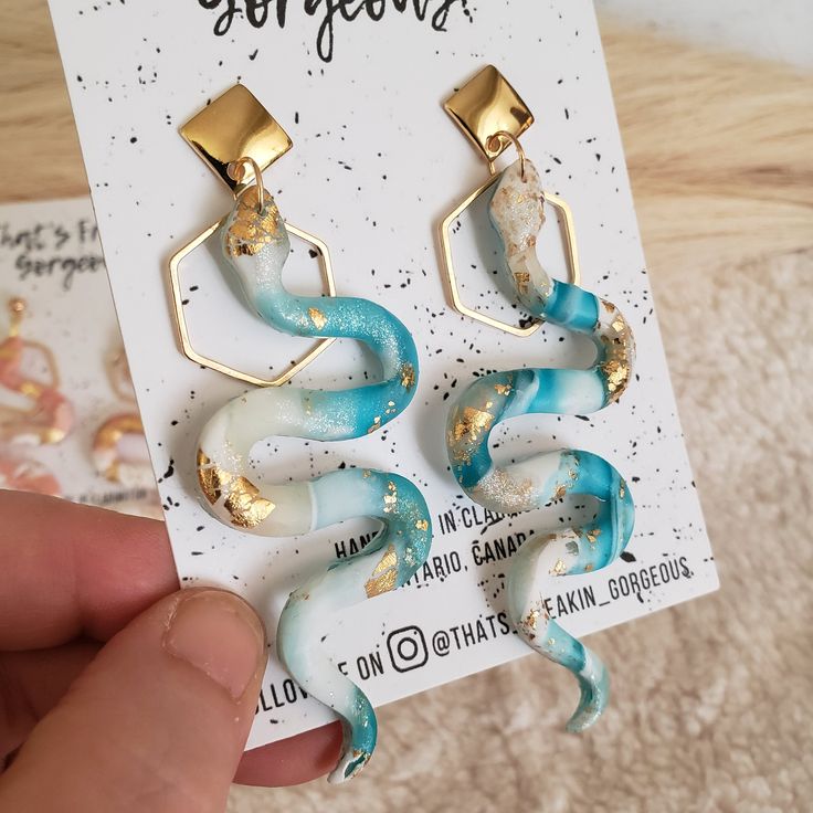 a pair of earrings with blue and white swirls on the front, gold accents