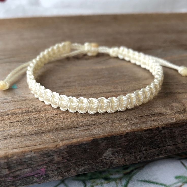 a close up of a string bracelet on a wooden surface with flowers in the background