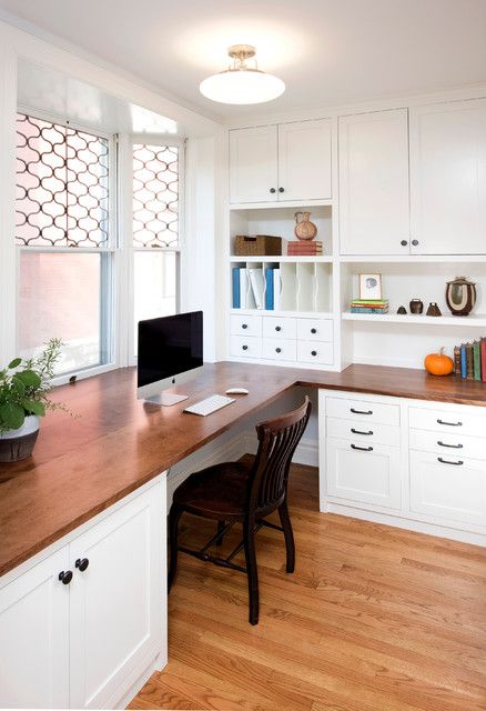 a desk with a computer on top of it in front of a window and bookshelf