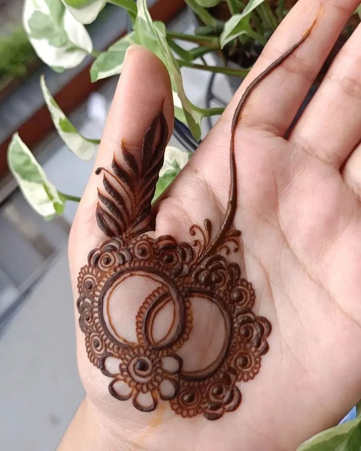 a hand holding a henna tattoo on it's left arm and palm with leaves in the background