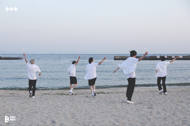 a group of young men standing on top of a sandy beach next to the ocean