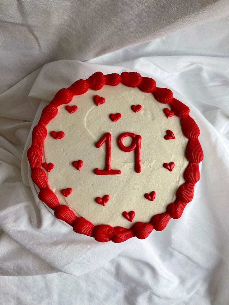 a red and white cake with the number 19 on it's side, surrounded by hearts