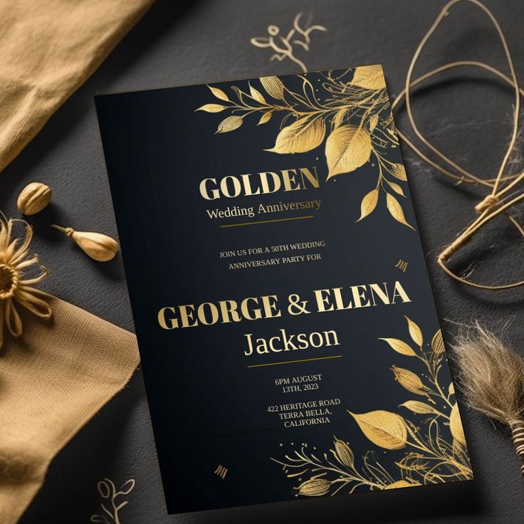 a black and gold wedding card on top of a table next to some flowers, feathers and other items