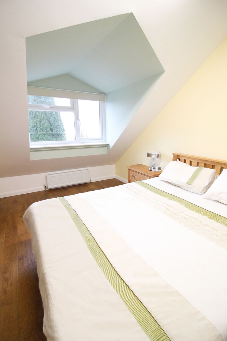 a bed with white sheets and pillows in a room that has an slanted ceiling