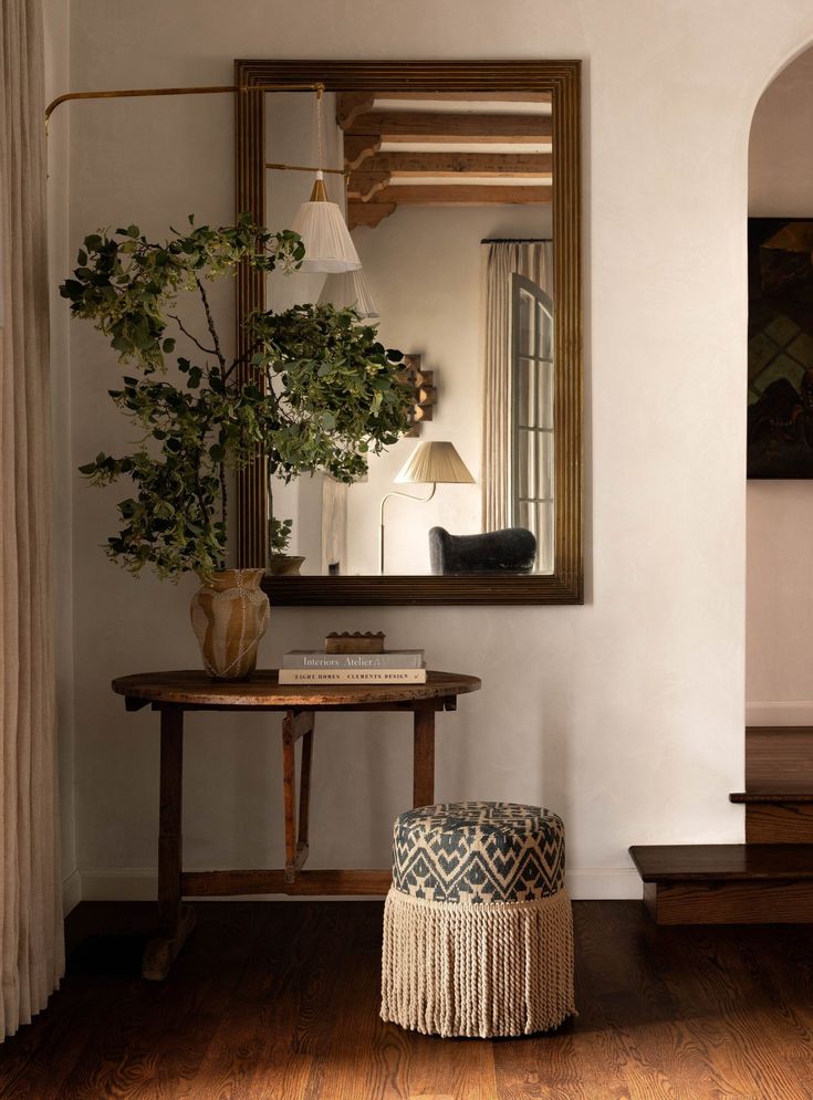 a living room with a mirror, table and plant on the wall next to it