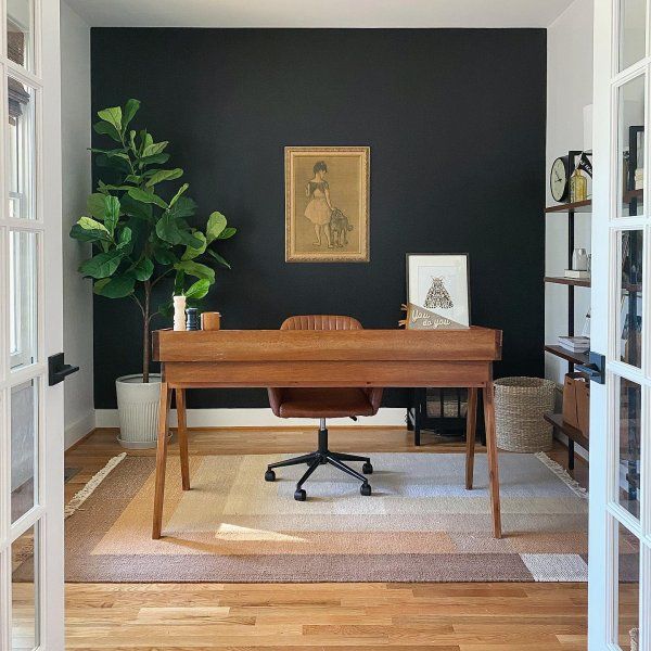 a home office with black walls and wooden desk in the center, surrounded by glass doors