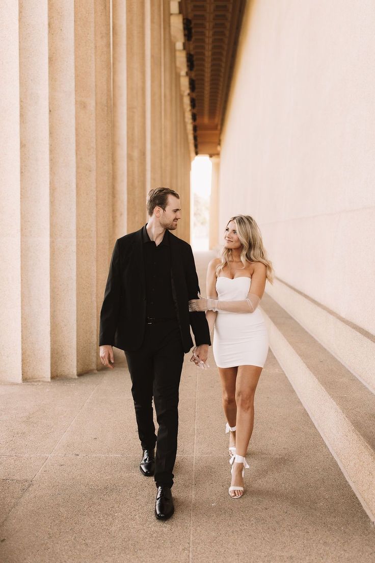 a man and woman holding hands walking down the street with columns in the back ground