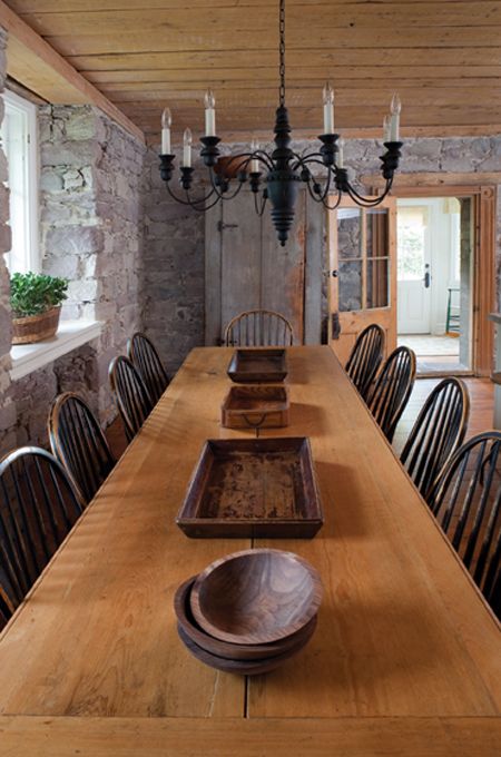 a long table with wooden chairs in a stone walled dining room, and an old - fashioned chandelier hanging from the ceiling