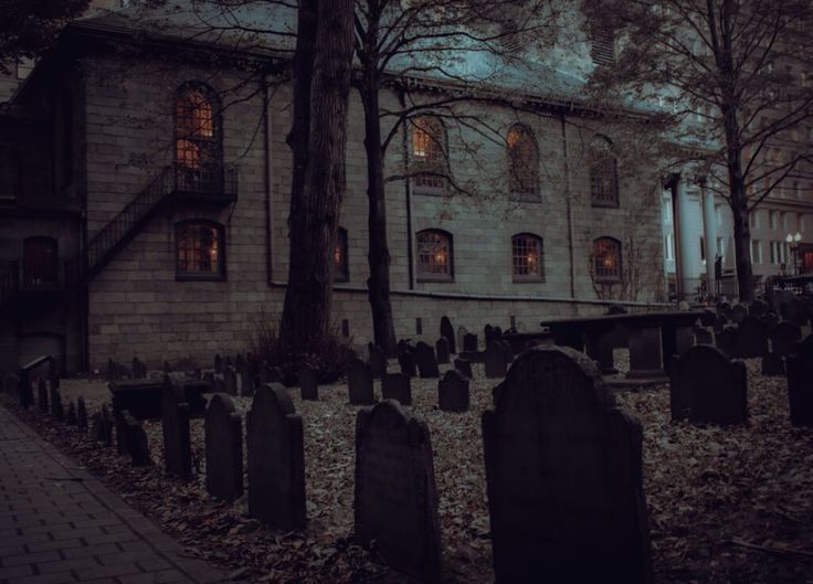 an old building with many headstones in front of it at night, surrounded by trees and leaves