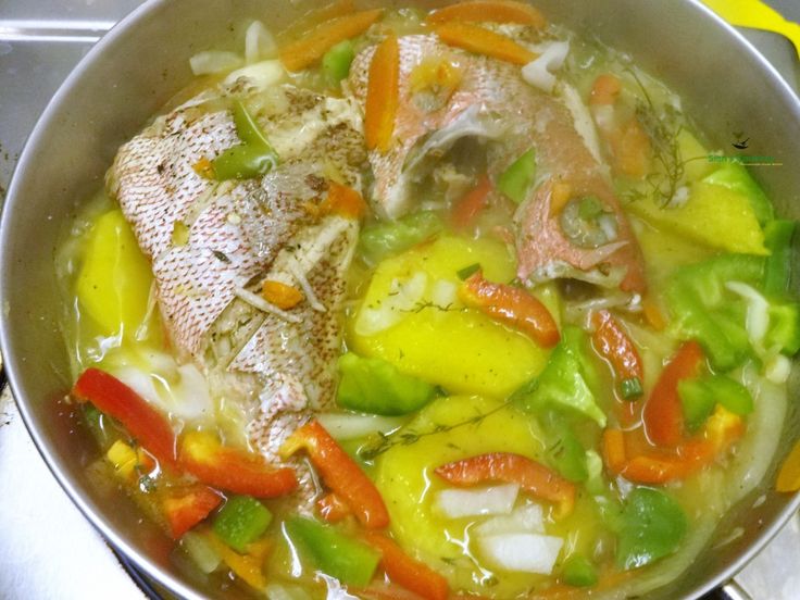 a pan filled with fish and vegetables on top of a stove