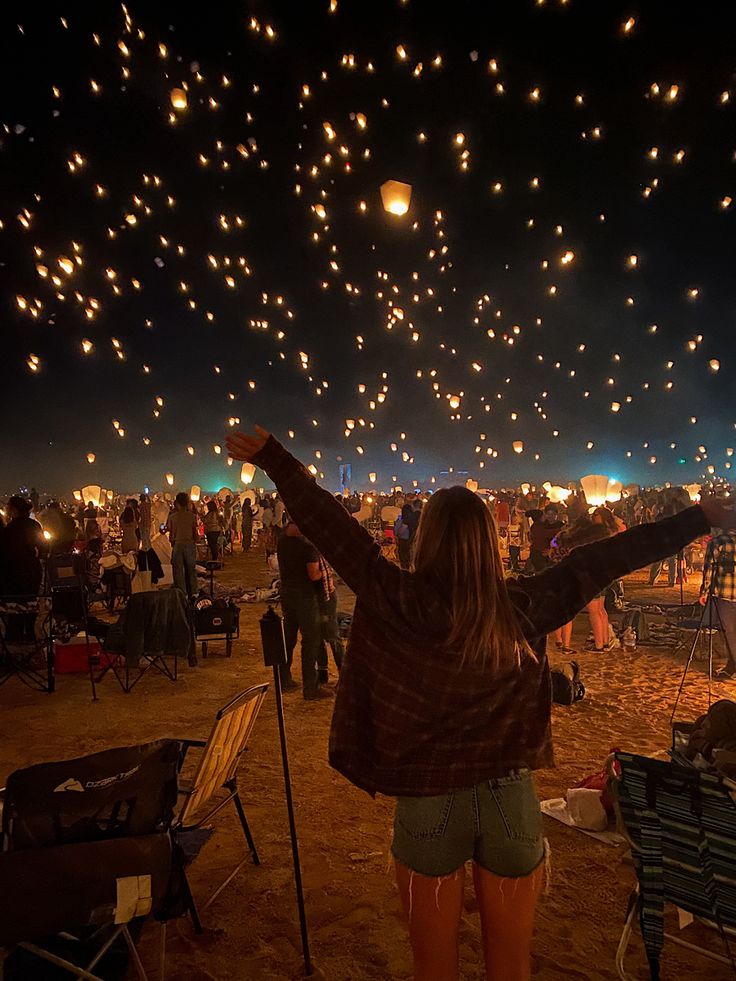 a woman is standing in the sand with her arms up and lights flying above her