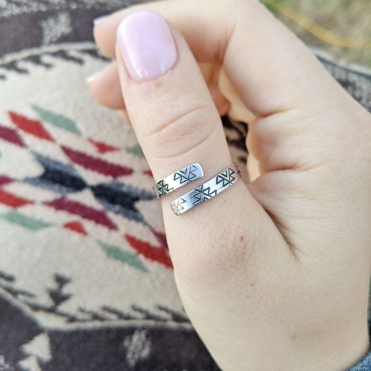 a woman's hand holding two silver rings with writing on the middle and bottom