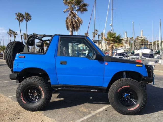 a blue pick up truck parked in a parking lot next to palm trees and boats