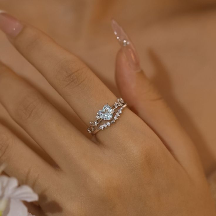 a woman's hand with a diamond ring on top of her finger and flowers in the background