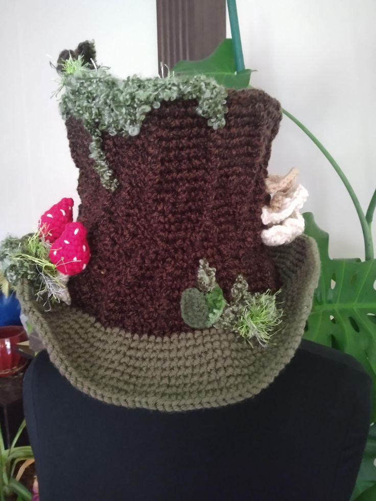 a crocheted hat with flowers and leaves on the top, sitting on a mannequin head