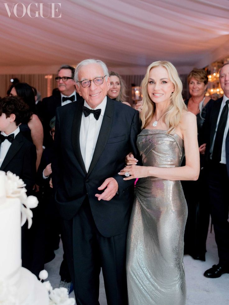 an older man and woman standing next to each other in front of a wedding cake