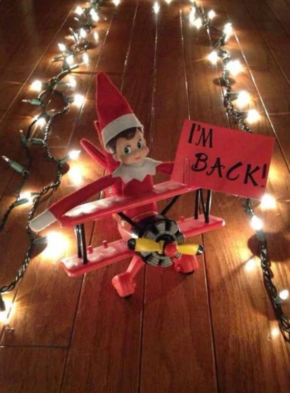 an elf sitting on top of a red plane with lights around it and a sign that says i'm back