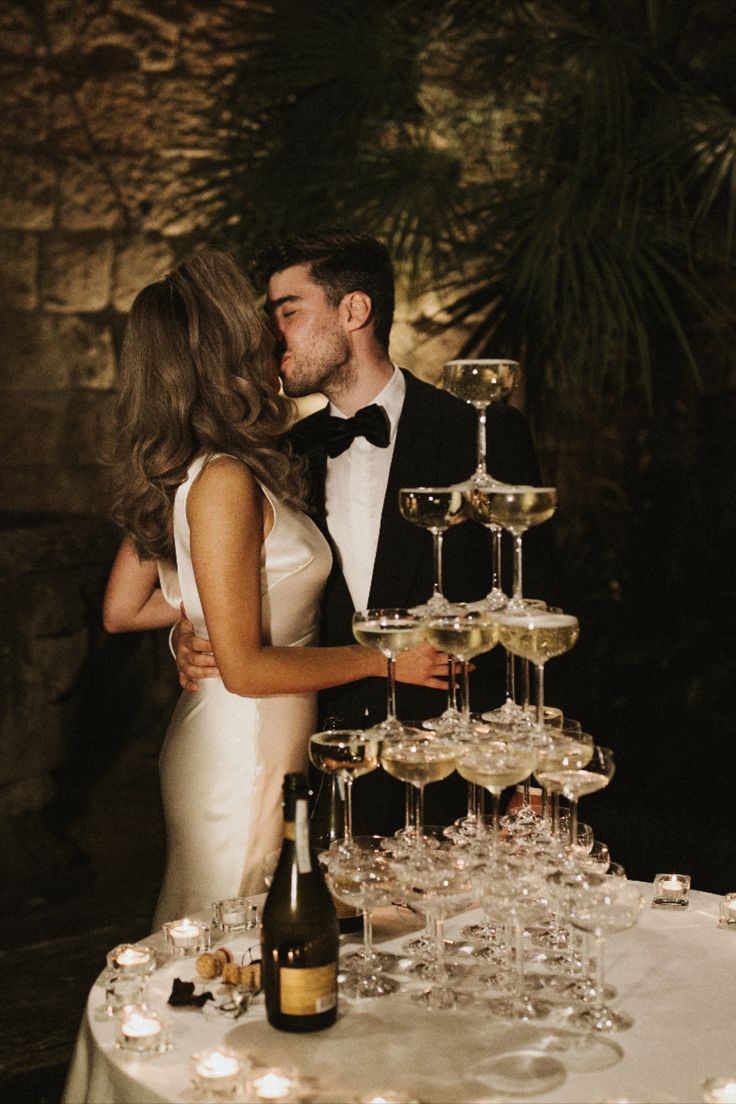 a bride and groom kissing in front of a table with wine glasses on it, surrounded by candles