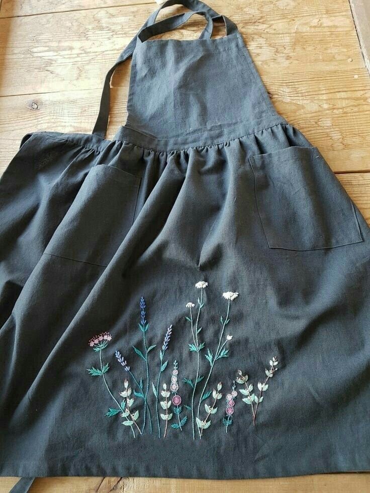 an apron with flowers embroidered on it sitting on a wooden floor next to a pair of scissors